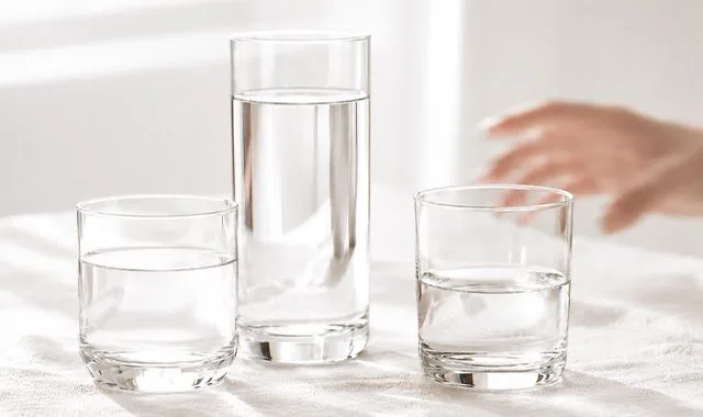 Trois verres d'eau fraîche de différentes tailles sur une table lumineuse